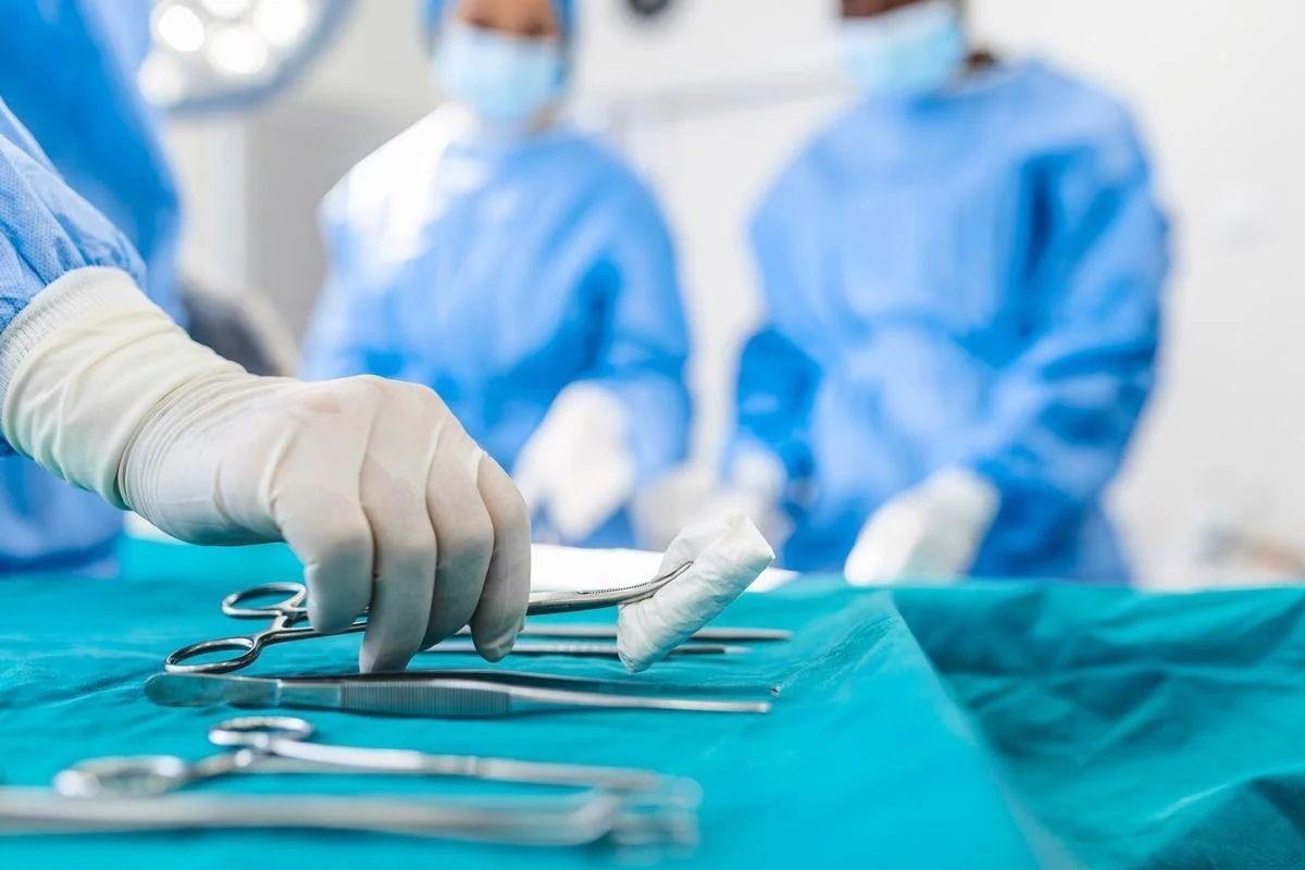 Surgical team in theatre with scissors, forceps and clamps laid out on a sterile drape